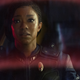 Commander Michael Burnham, in Discovery away team gear, looks out of a viewport with a face of concern.